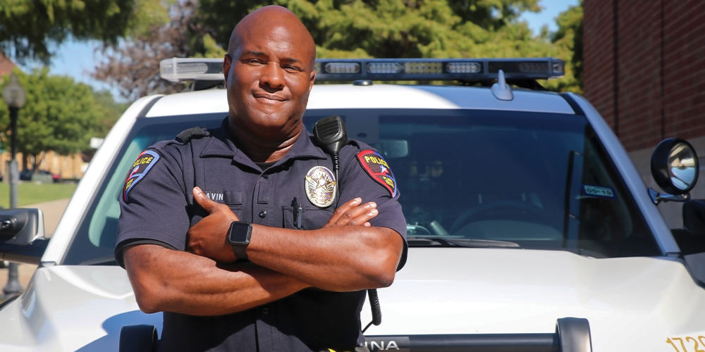 Black police officer with folded arm poses in front of his squad car