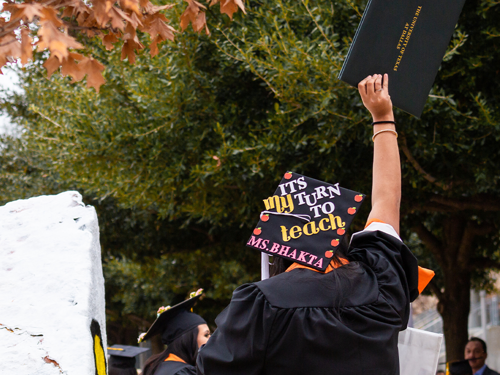 Woman waving diploma holder with a cap that says it’s my turn to teach