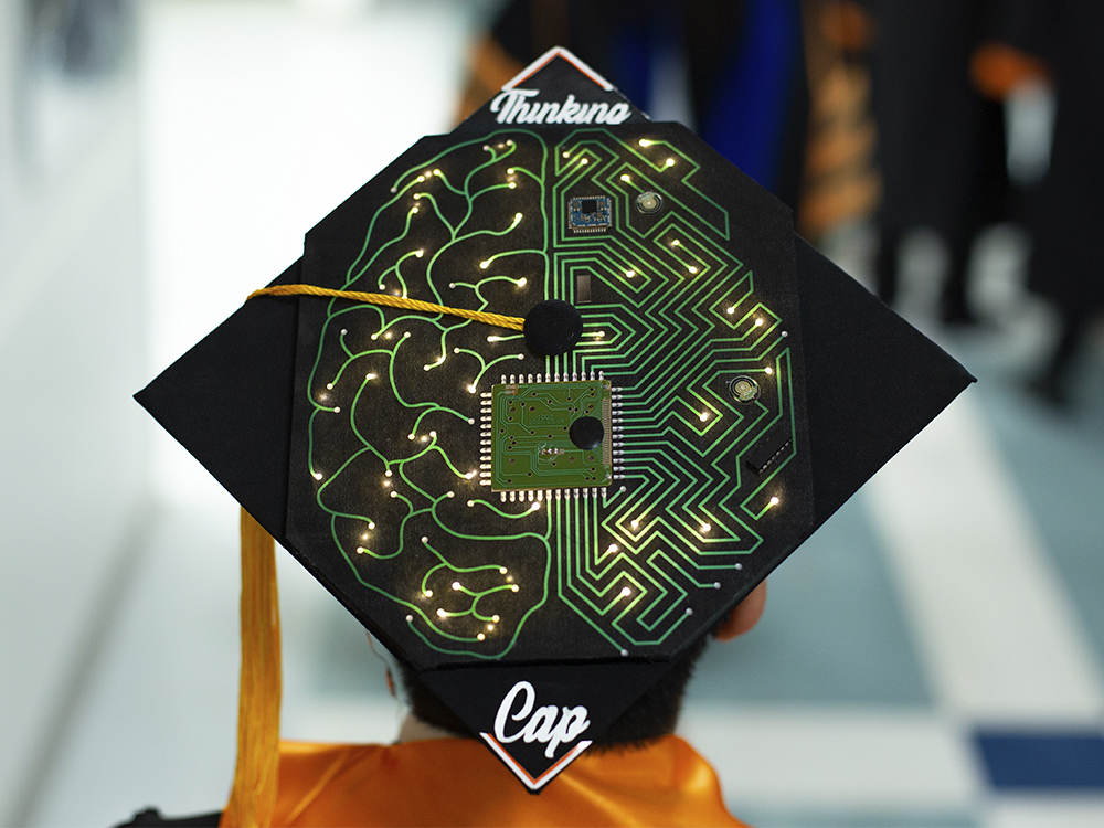 Man wearing cap that says thinking cap and has an image of a brain as a circuit board