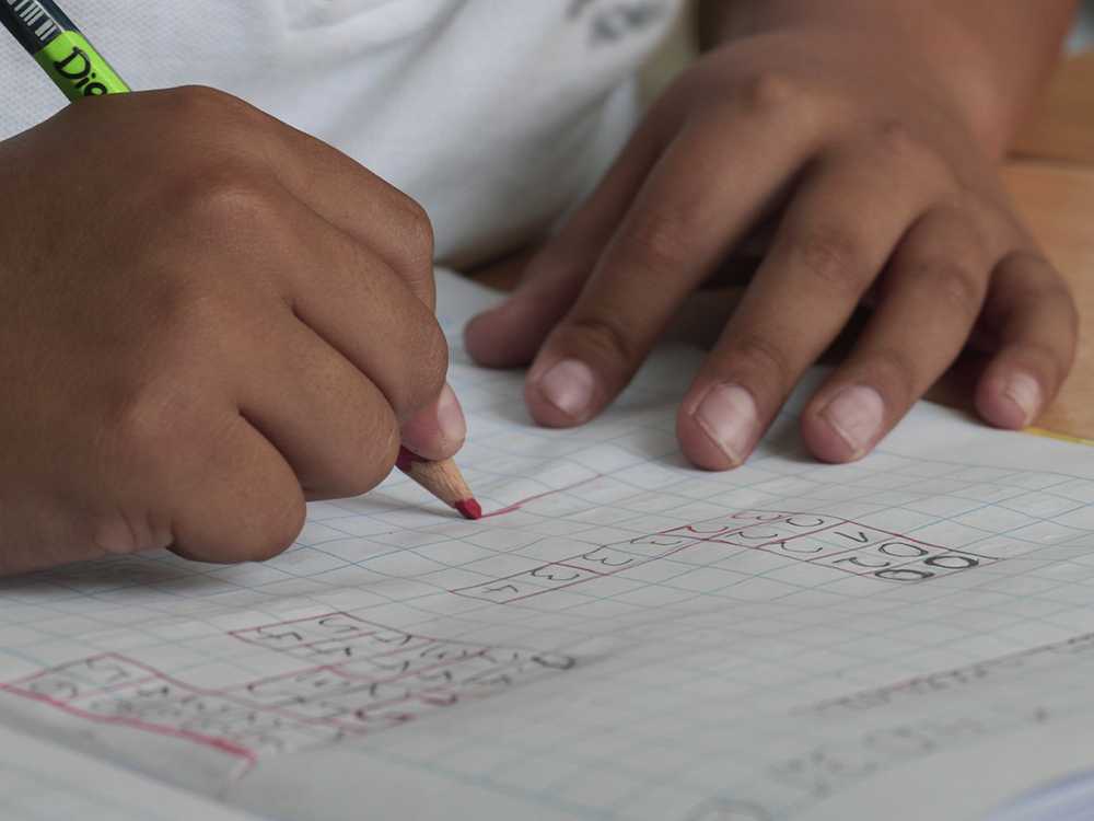 Young student fills out a math problem on a piece of paper with a red pencil