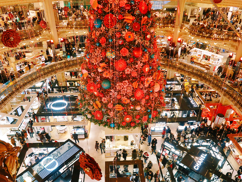 A giant red holiday tree surrounded by vendors and shoppers in a mall.