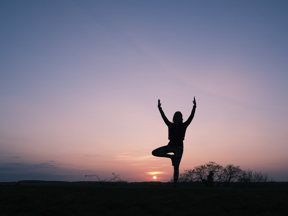 Silhouette of a person doing a yoga pose as the sun sets.