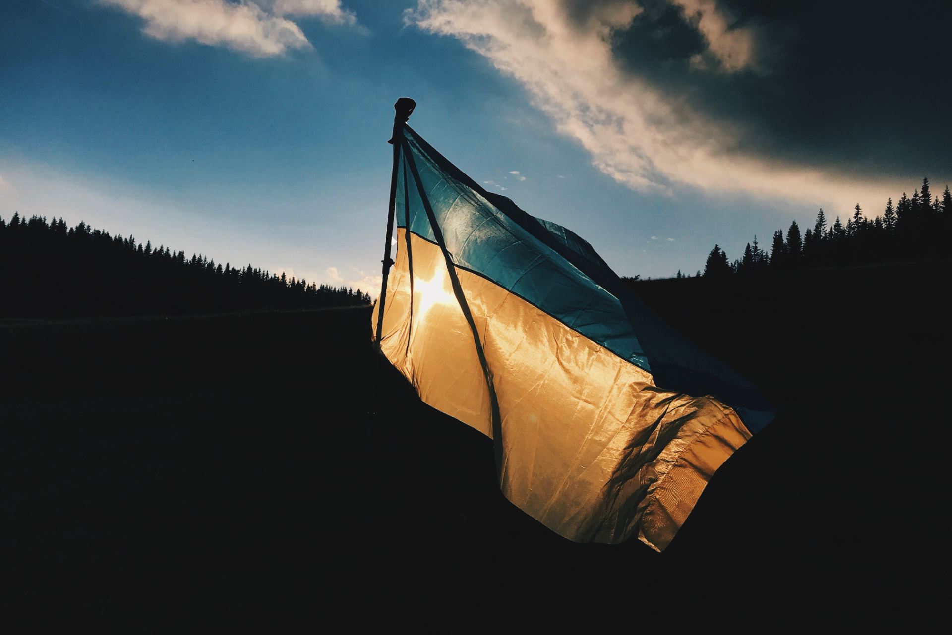 Sun shines through the blue and yellow of a waving flag of Ukraine.