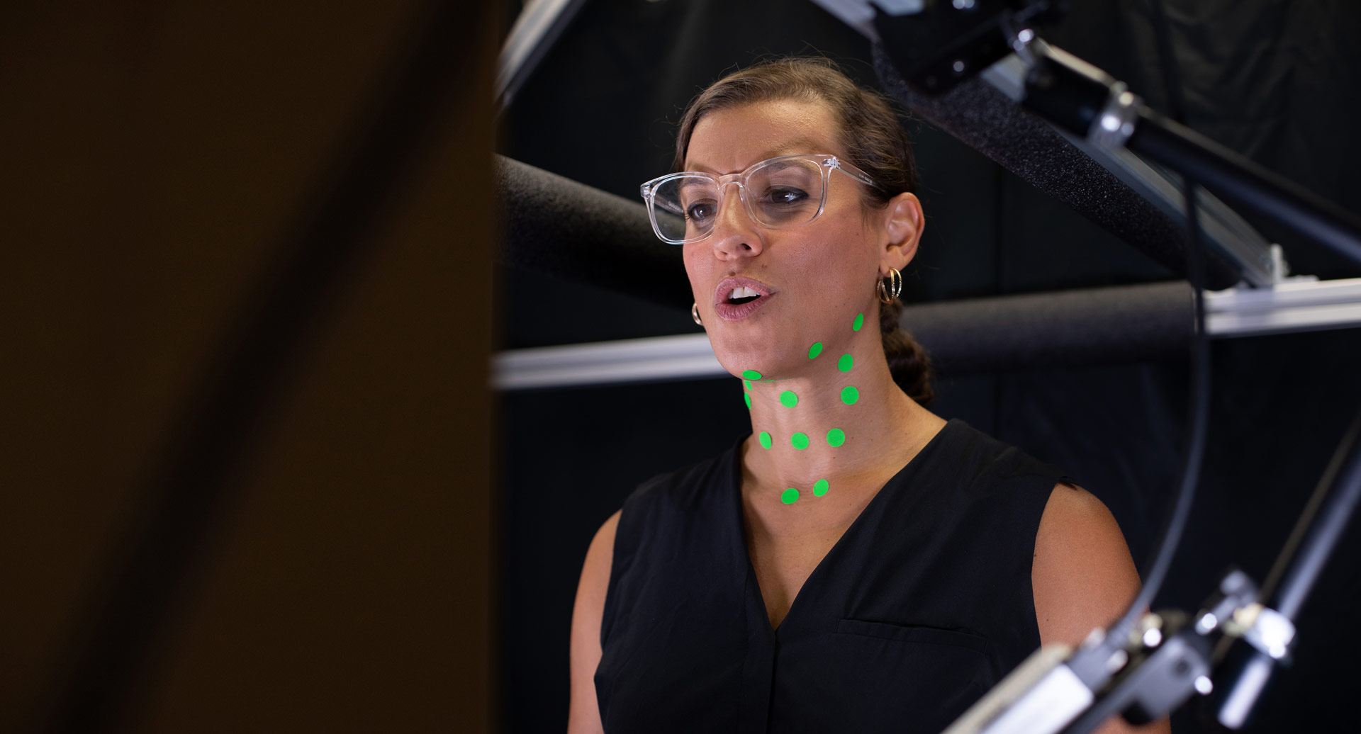 Adrianna Shembel singing. She has green dots affixed to her chin and neck.