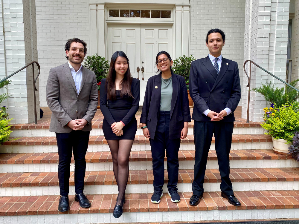 Four students dressed in business attire stand on red steps for a photo.