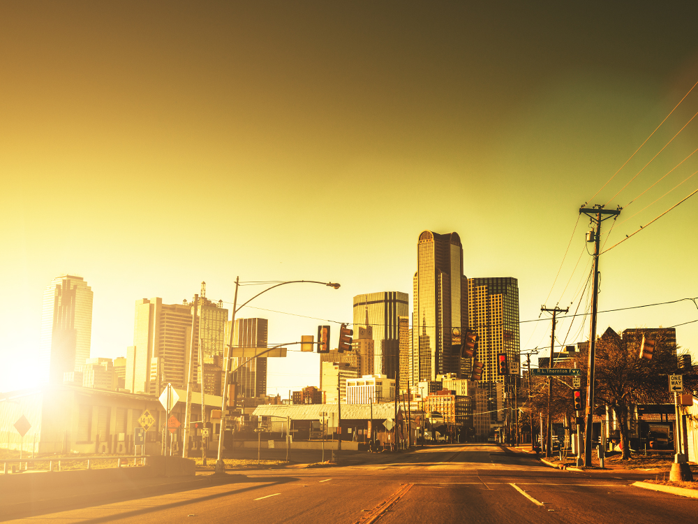 An image that shows downtown Dallas, Texas with the sun near the horizon, causing brightness and warm light on the buildings and street
