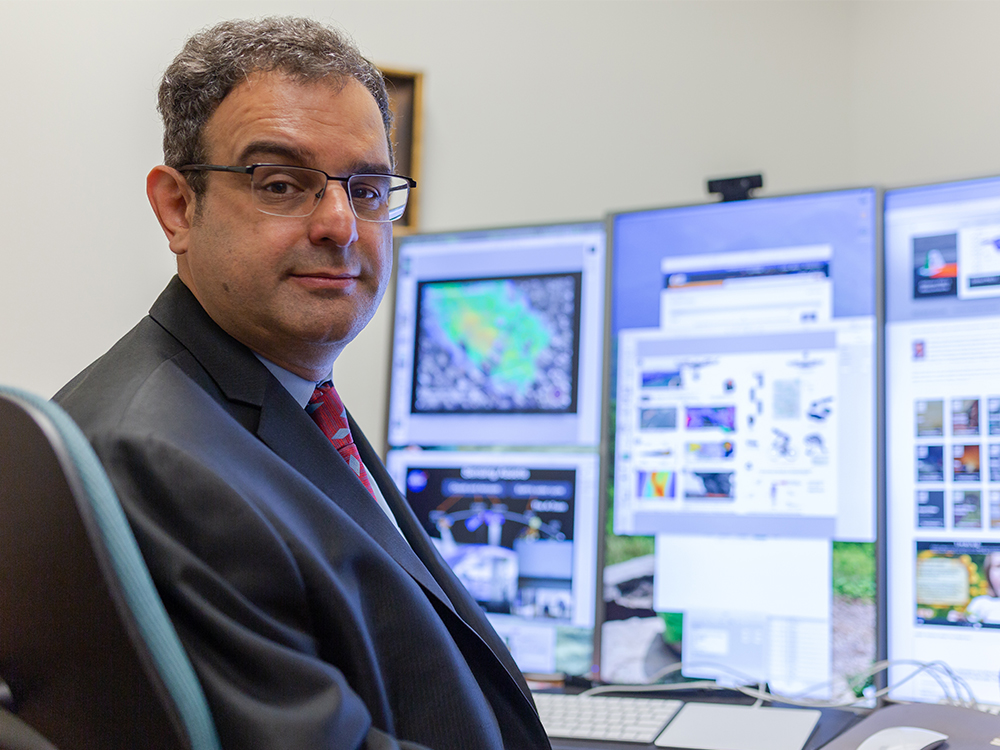 Dr. David Lary sits at his desk with computer monitors on top, looking back at the camera