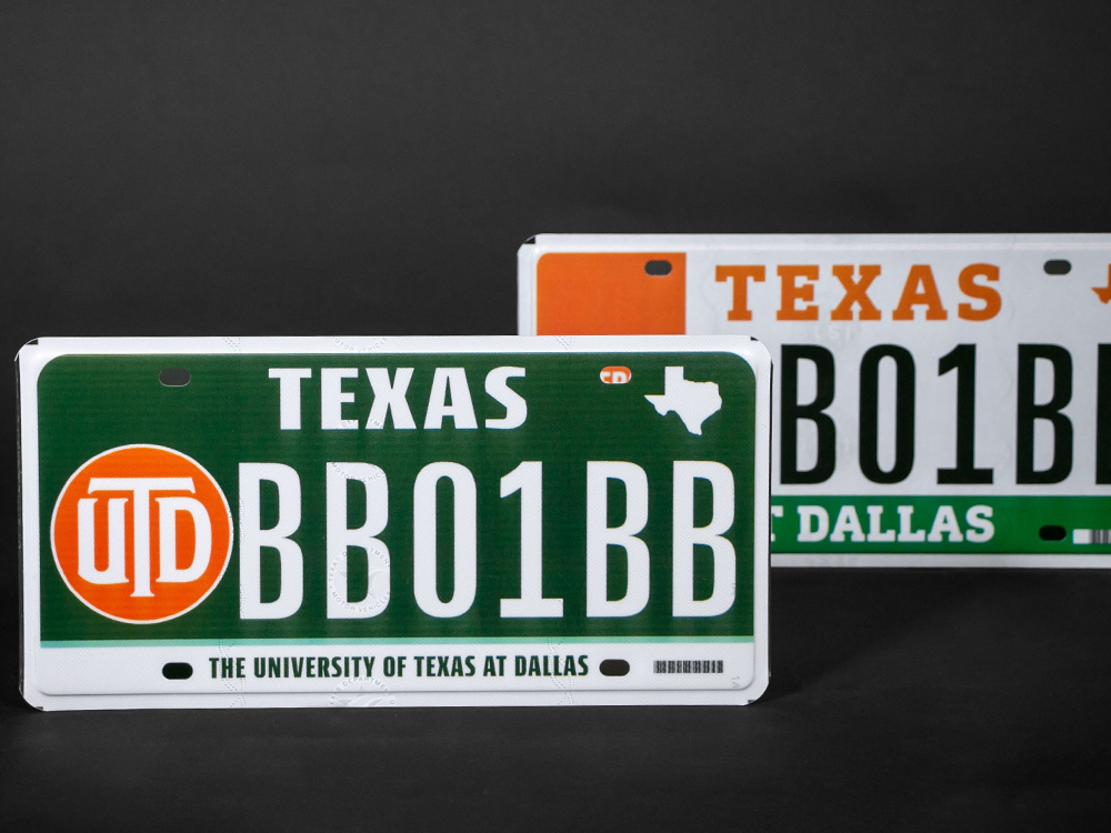 The new UTD license plate, with a green background and orange U-T-D monogram, sits in front of the old design.