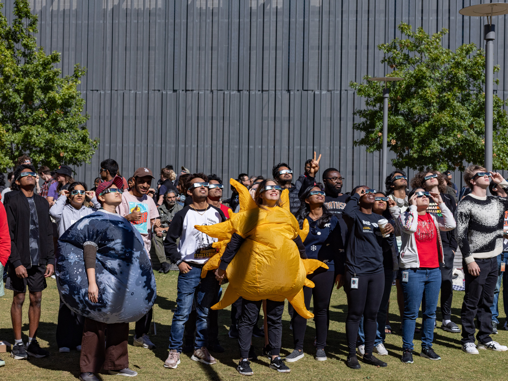 people gathered on the UT Dallas campus with solar eclipse viewing glasses looking up at the sun during the October 2023 partial solar eclipse